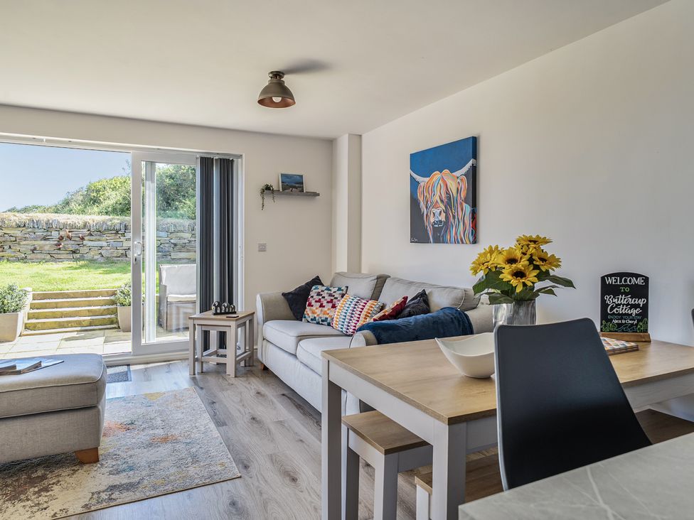 A living room with a sofa and dining table at Buttercup Cottage St Merryn