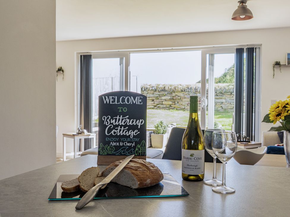 A dining room with a welcome sign and a bottle of wine at Buttercup Cottage St Merryn