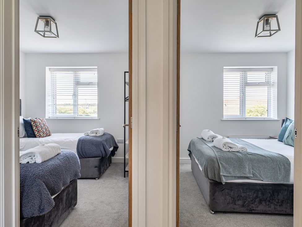 A bedroom with two beds and windows at Buttercup Cottage in St Merryn