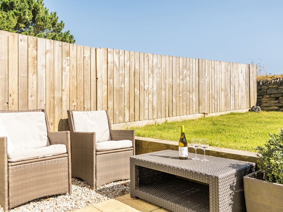A garden with chairs, coffee table, and wine at Buttercup Cottage St Merryn