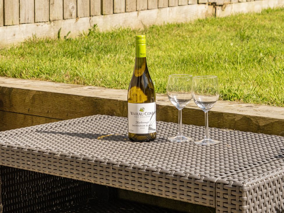 A bottle of wine and two glasses on a table in the garden at Buttercup Cottage St Merryn