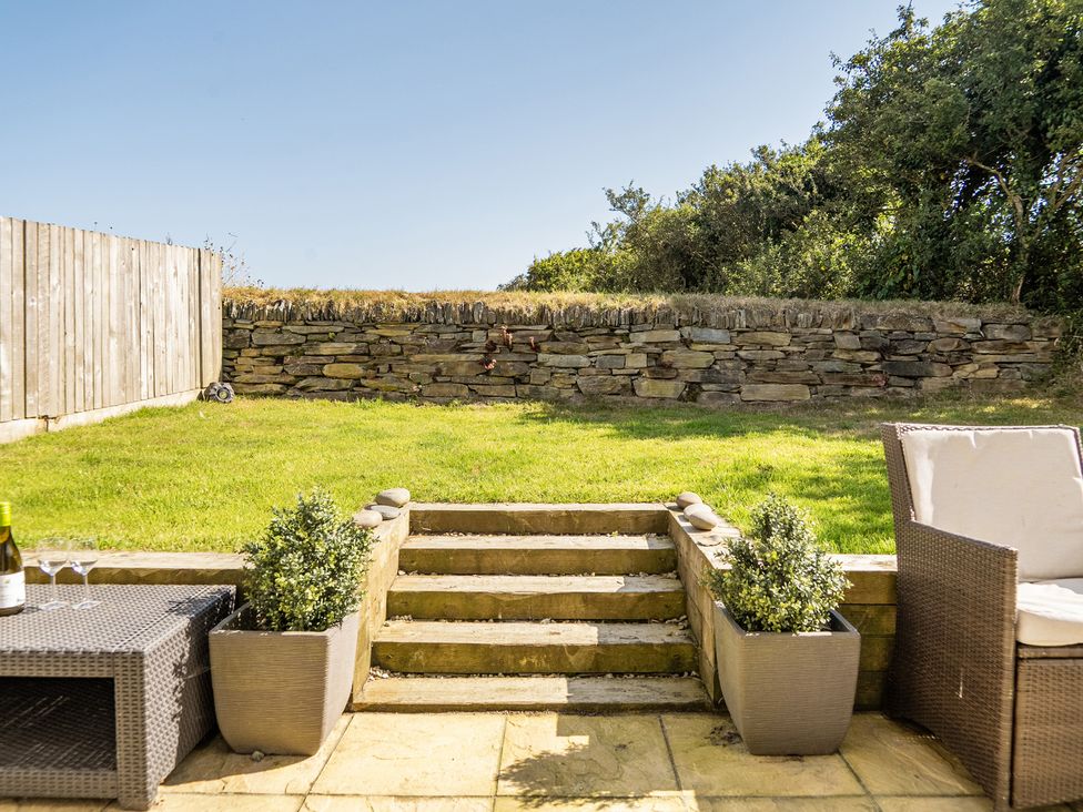 A garden with grass, stone wall and outdoor furniture at Buttercup Cottage in St Merryn