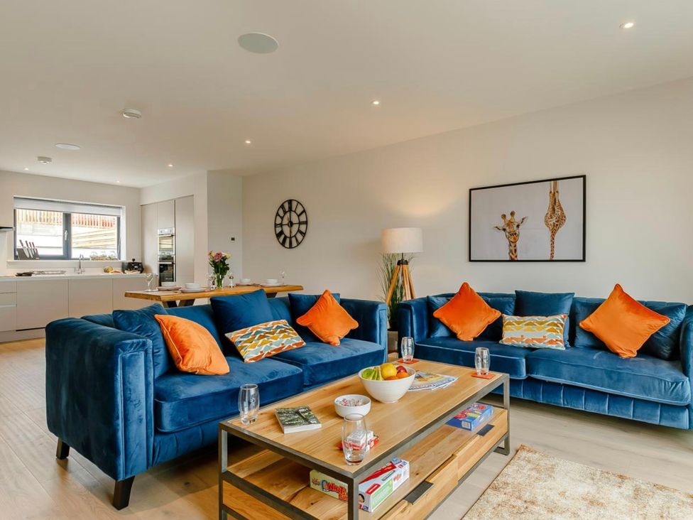 A living room with sofas, a coffee table, and a kitchen in Seascape Newquay