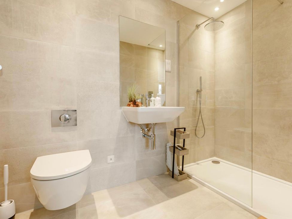 A bathroom with a toilet, sink, shower and mirror at Seascape in Newquay