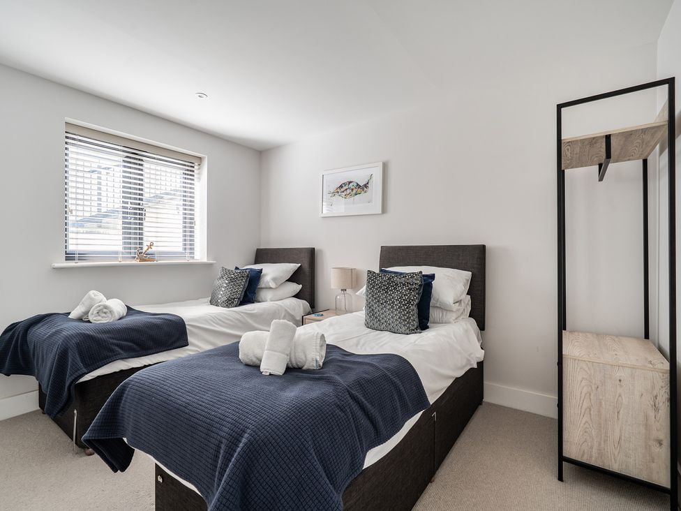 A bedroom with twin beds, window, and shelf unit at Seascape in Newquay