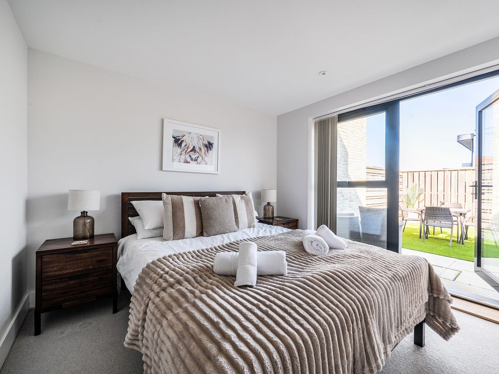 A bedroom with a bed, bedside tables, and a door leading to an outdoor area at Seascape in Newquay