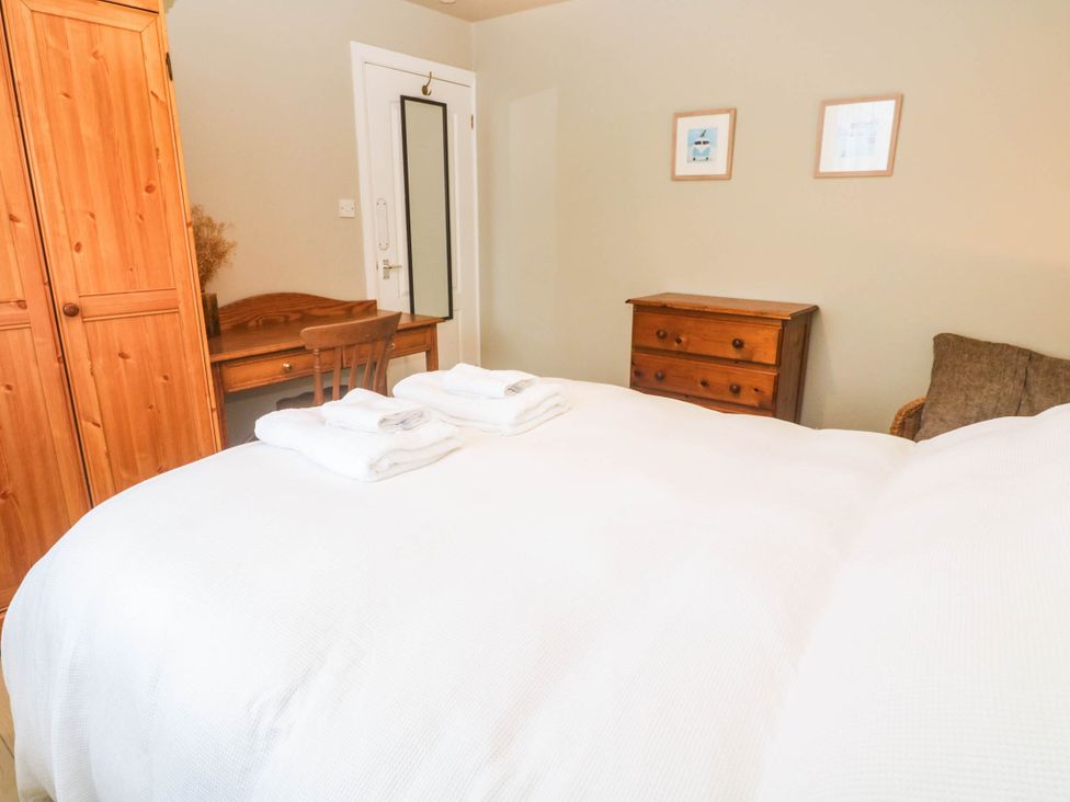 A bedroom with a bed, wardrobe, table, and chair at 8 Yellow Sands in Padstow
