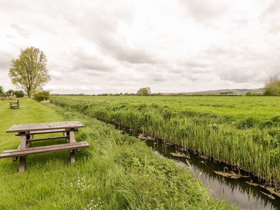 A picnic table and benches near a stream in a field at Oak Tree in Weston-super-Mare