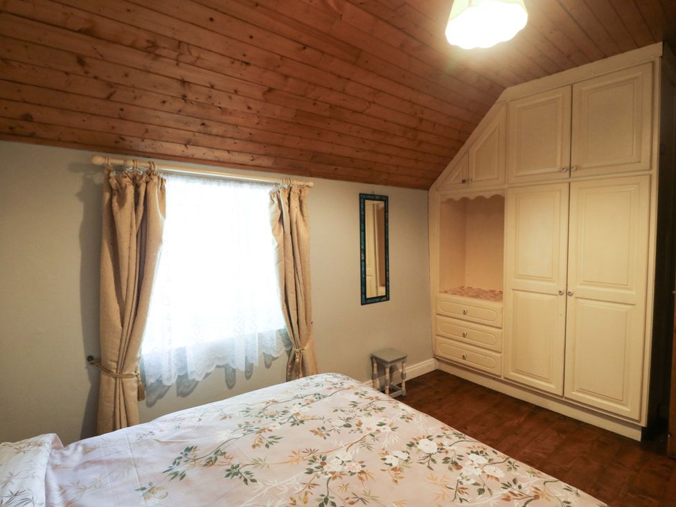 A bedroom with a bed, curtains, a window, and a wardrobe at Gullane East in Rathmore, County Kerry