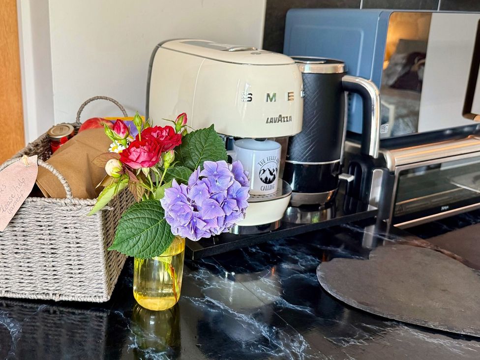 A kitchen with a coffee machine, kettle, and flowers at La'al Yan in Branthwaite