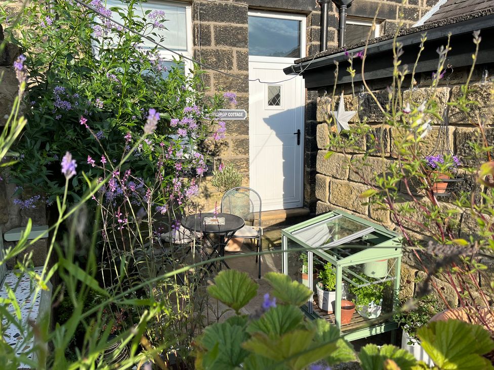 A garden with a table and chairs and greenhouse at Snowdrop Cottage in Cowling