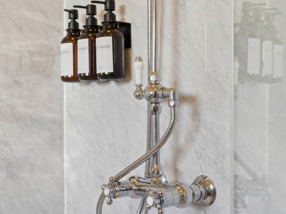 A shower with a chrome faucet and bottles at 5 Acres Cottage in Rickmansworth