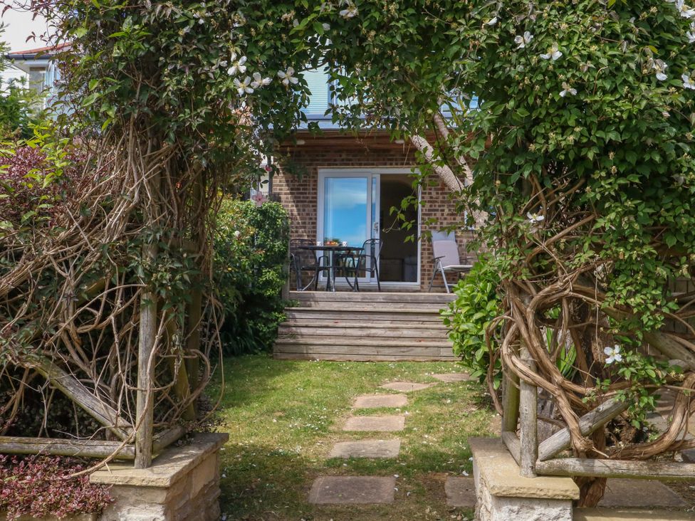 A garden with a pathway leading to a patio area at Little Gem in Weymouth