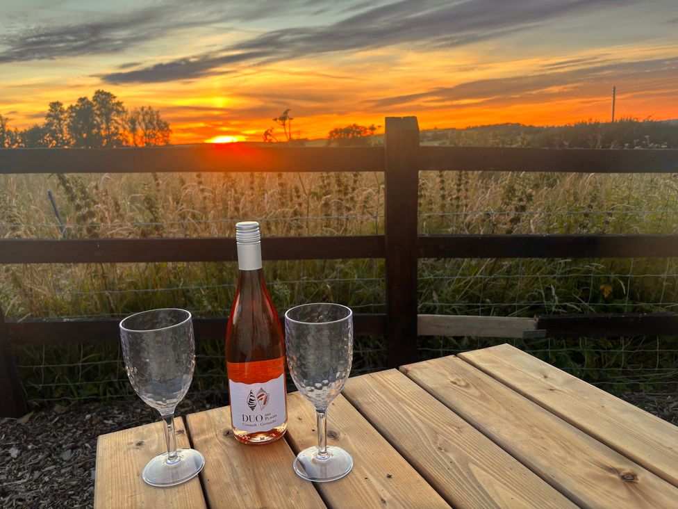 A wooden table with wine glasses and a bottle during sunset at Cider Cottage near Launceston