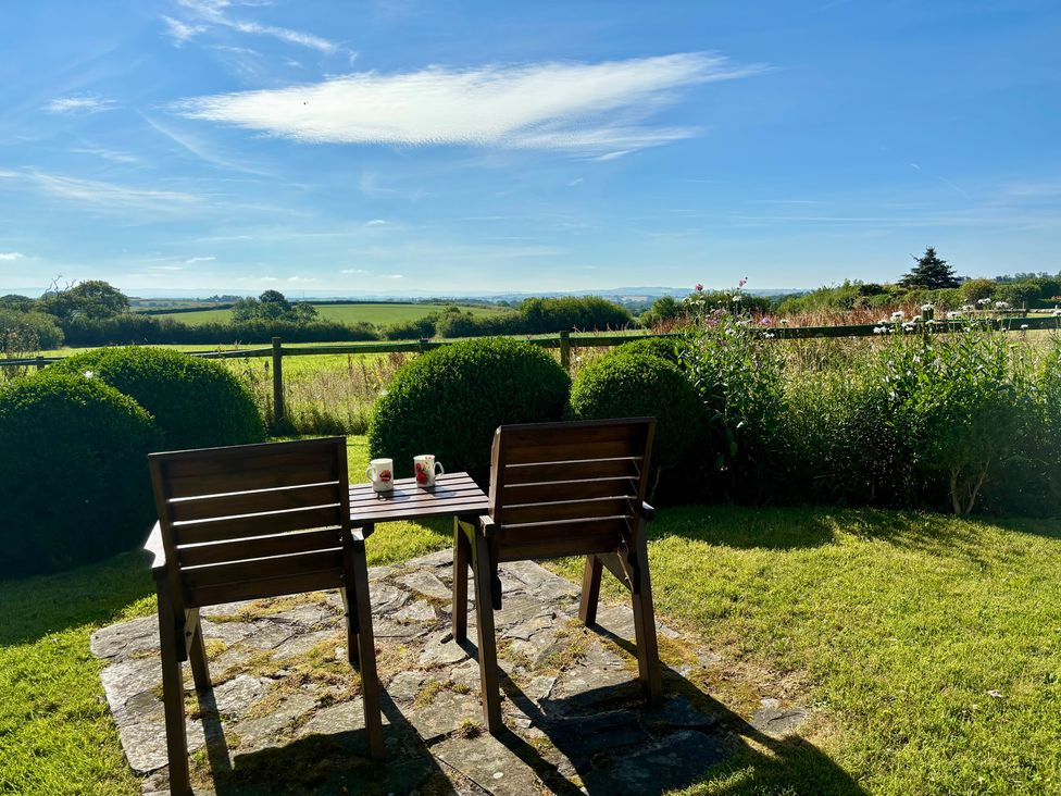 A garden with chairs and a table overlooking a field at Cider Cottage near Launceston