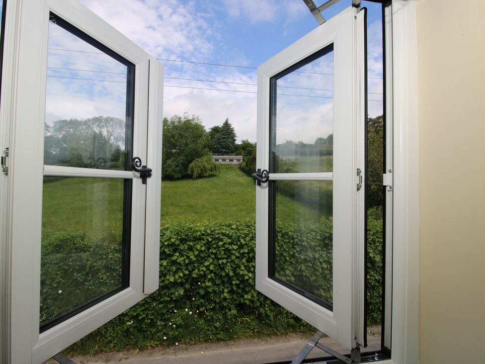 A view from an open window showing grass and trees at The Dinky Dairy in Treflach near Trefonen