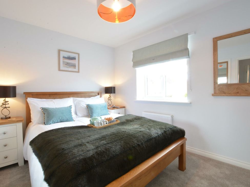 A bedroom with a bed, nightstands, lamps and a window at Lapwings, Aldeburgh
