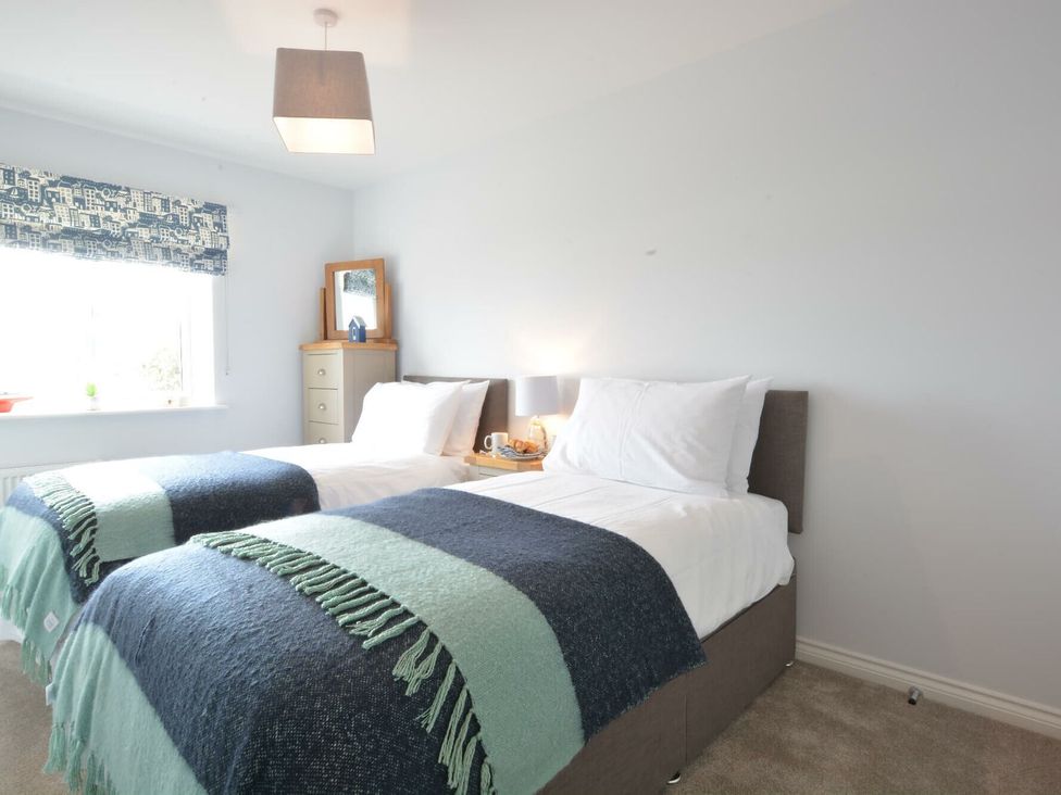 A bedroom with two beds, a nightstand, and a window at Lapwings, Aldeburgh