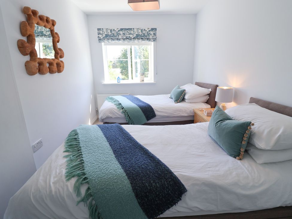 A bedroom with two beds and a lamp on a nightstand at Lapwings, Aldeburgh