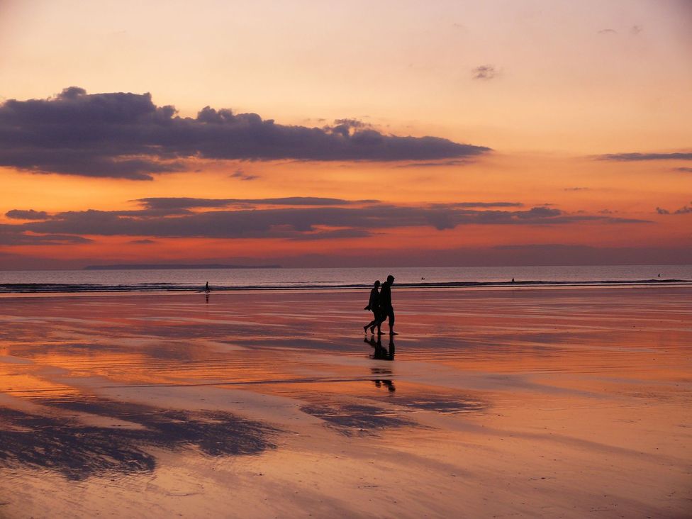 A beach during sunset with people walking at Whitefield Cottage in Barnstaple
