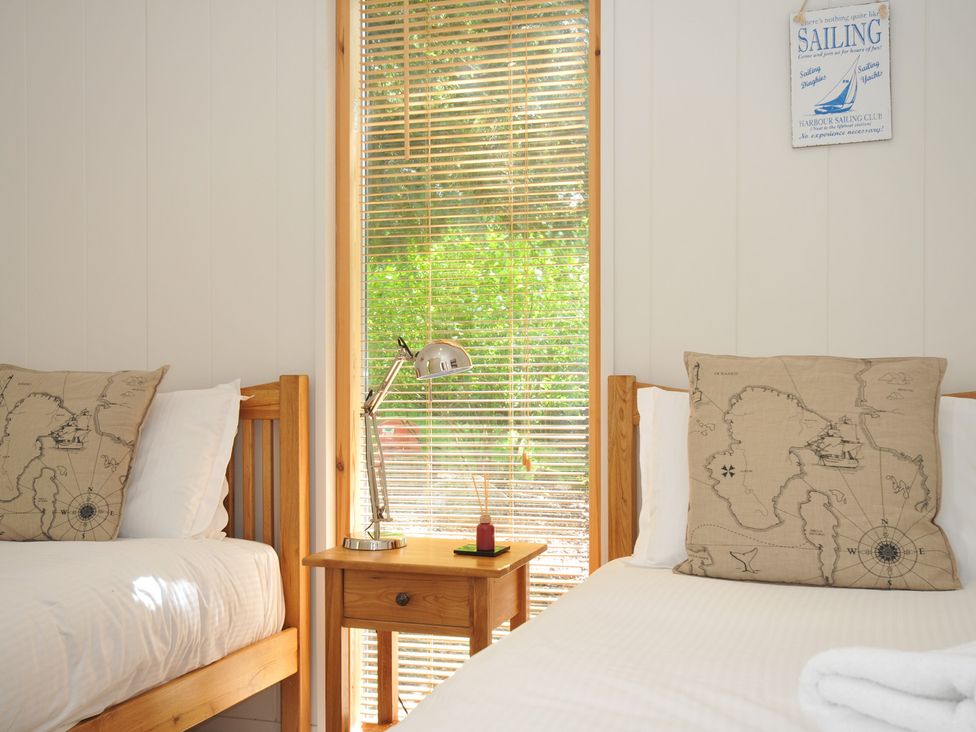 A bedroom with two beds and a lamp on a wooden table at 11 Water's Edge near Pelynt