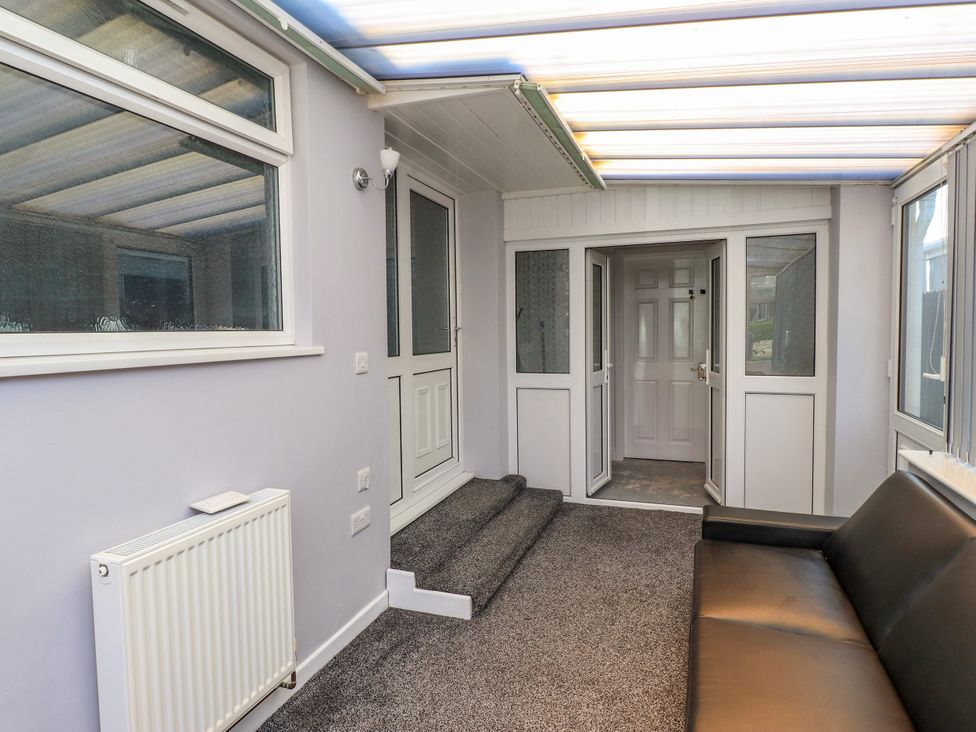 A conservatory with a sofa and door at Ger y Mynydd, 2 Cae Ty Coch, Brynteg