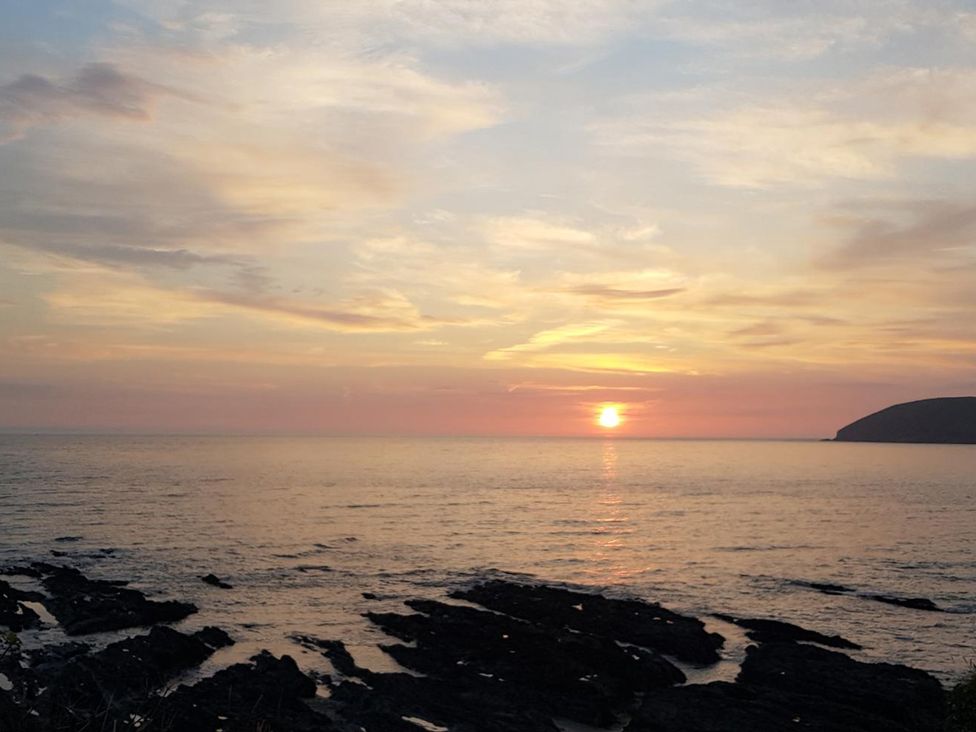 A sunset over the ocean with rocks visible at Dingle Dell in Croyde