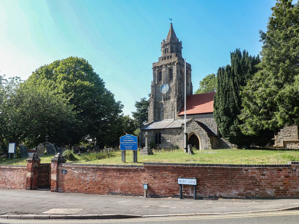 A church with a clock tower and gravestones at Selby Lane in Nottingham