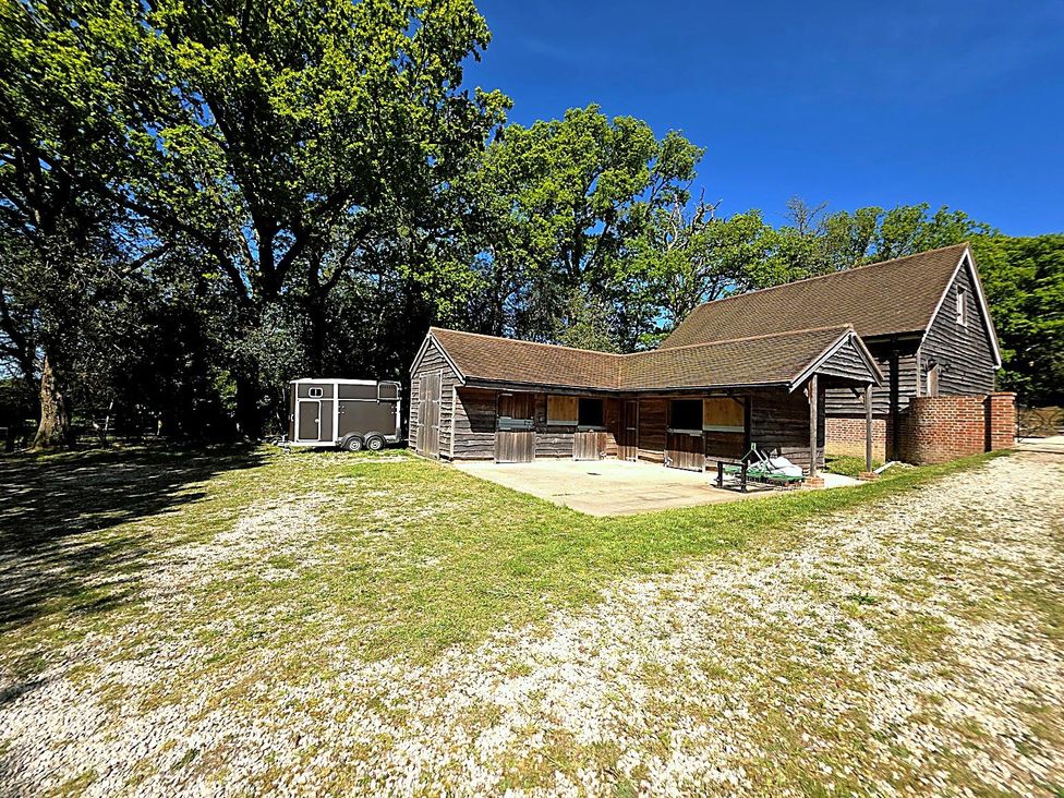 A barn and stables with trees in the background at Charming Barn Annex with Stables New Forest Escape