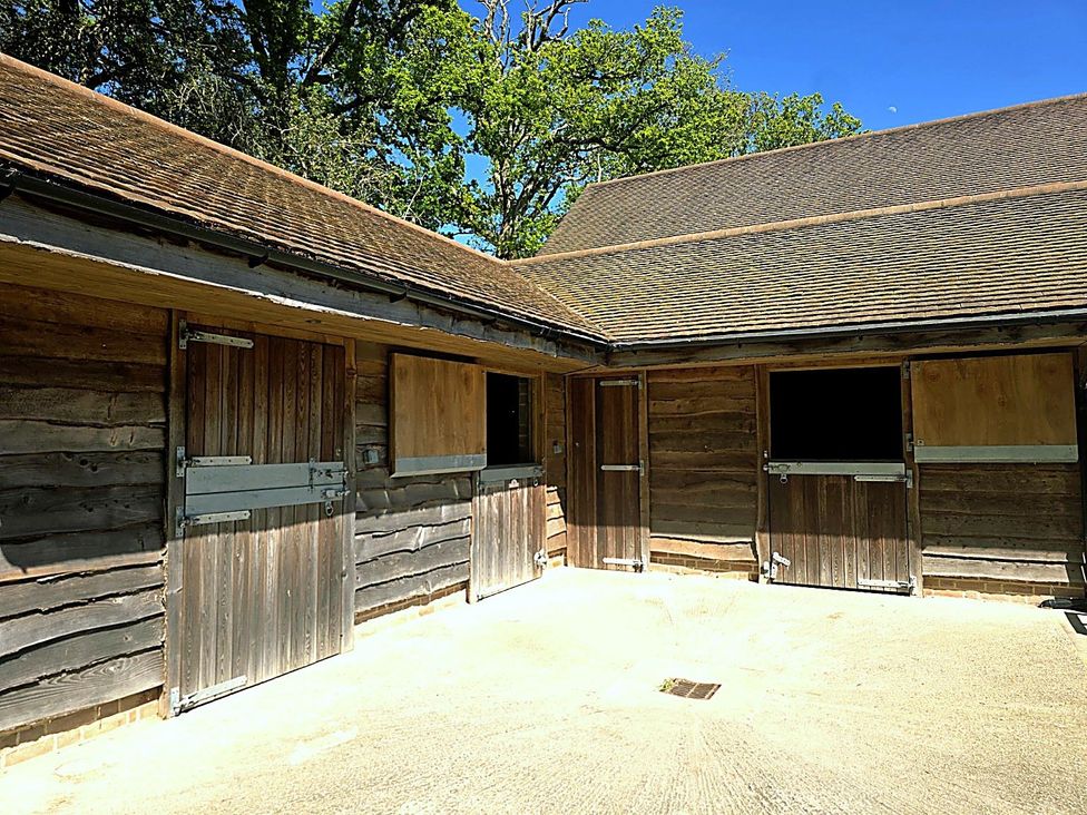 A stable with wooden doors and a concrete floor at Charming Barn Annex with Stables New Forest Escape