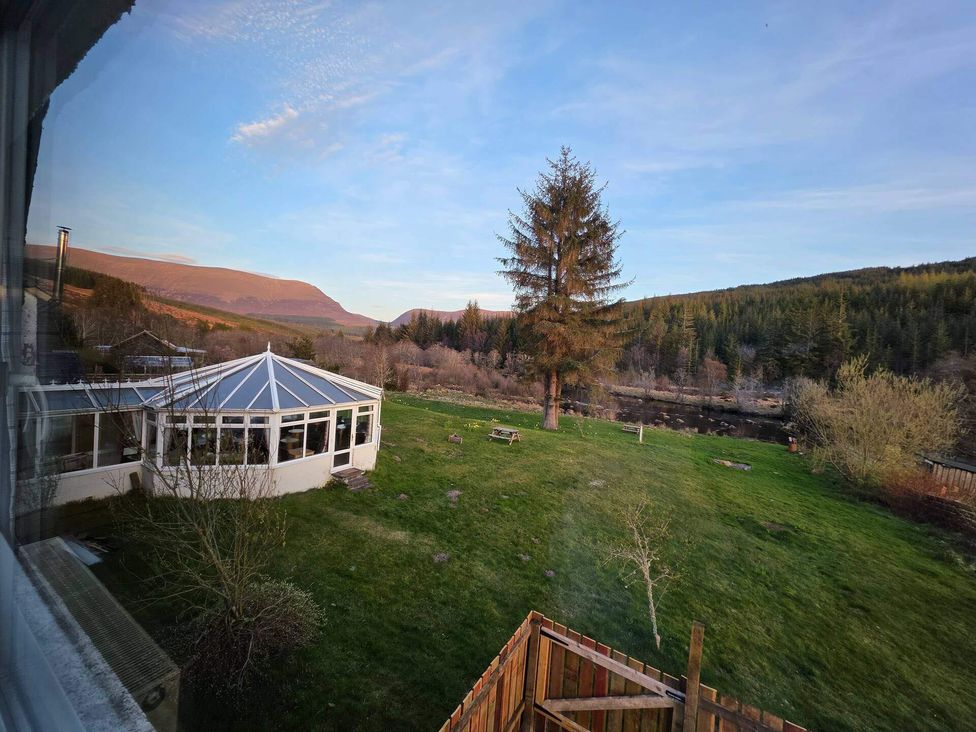 A garden view with a conservatory and a tree at Highlands - River View - Apt - Sleeps 4 - Garden in Garve near Strathpeffer