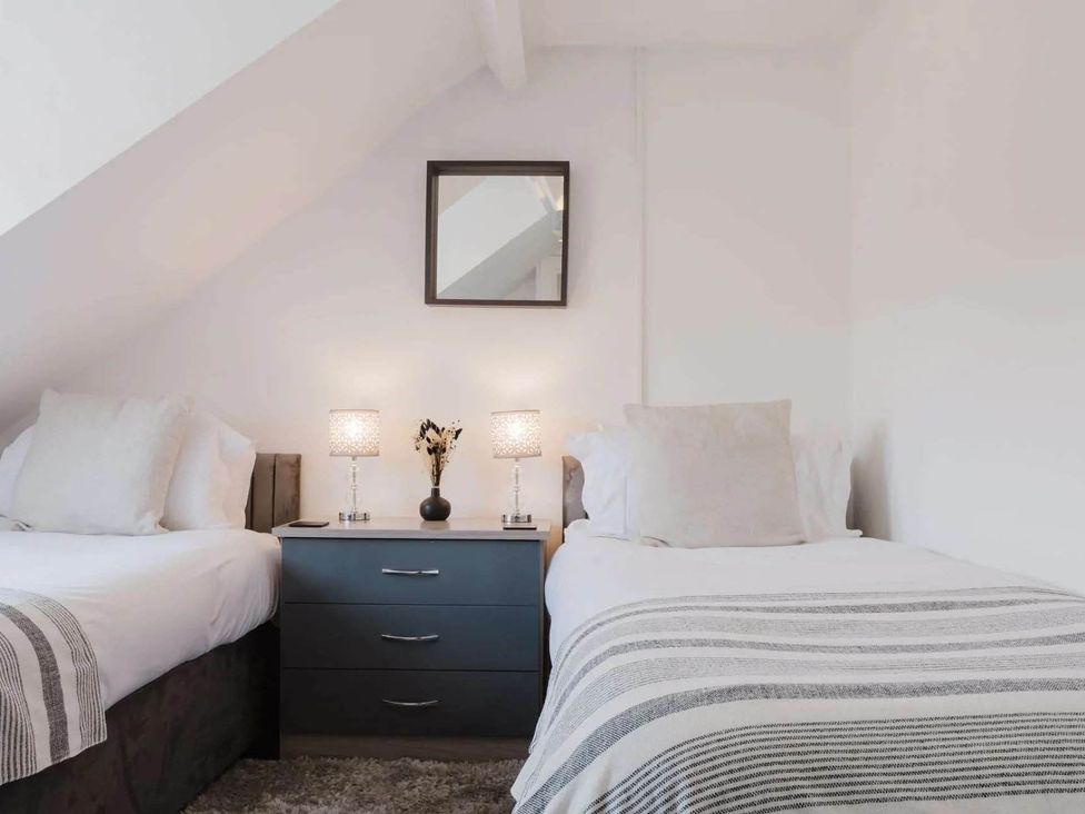 A bedroom with two beds and a nightstand at Licatas Apartment Cirencester Cotswolds Sleeps 6