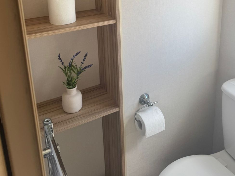 A bathroom with a toilet and shelves containing a plant at Caravan - Sleeps 6 - Parking in Lossiemouth
