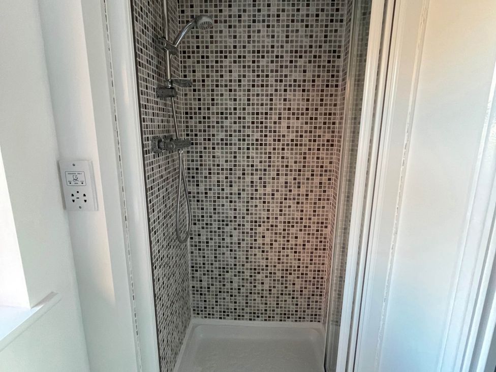 A shower with mosaic tiles and shower head at House Sleeps 5 with Garden and Parking