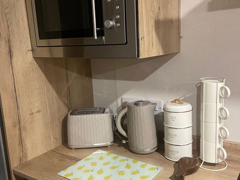A kitchen with a microwave, toaster, kettle, and storage canisters at Coworth Deluxe Cabin with Garden
