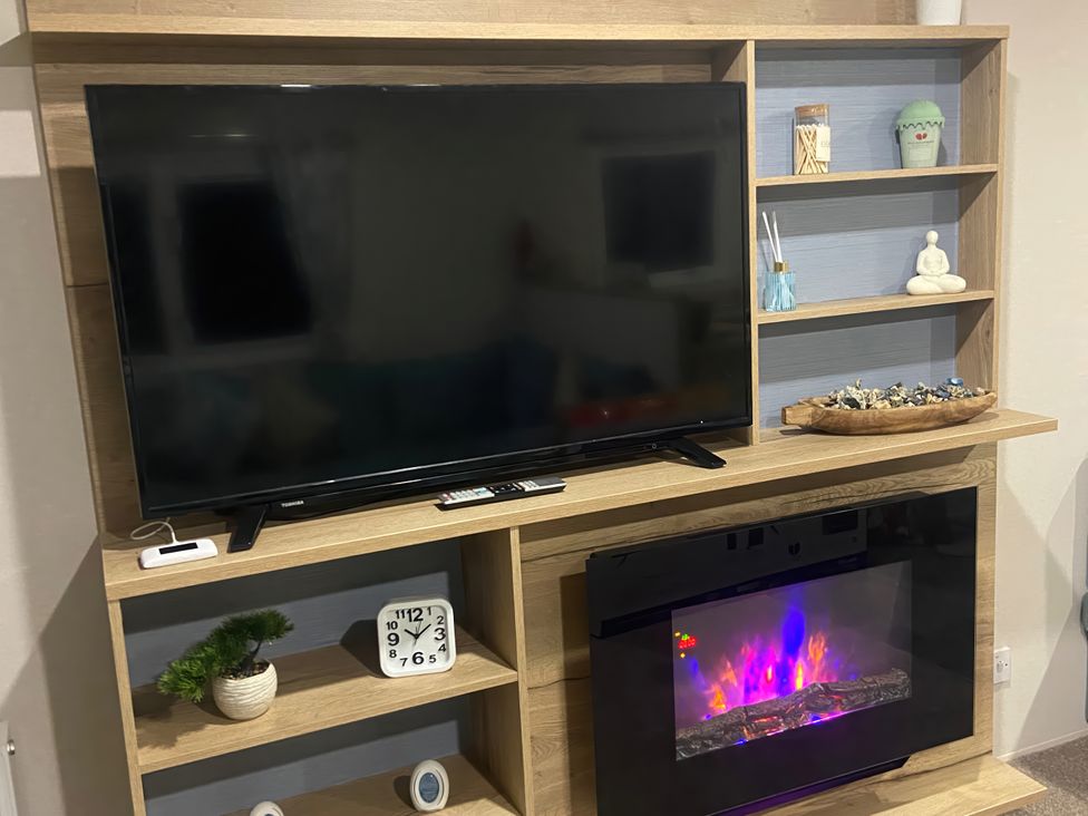 A living room with a television and electric fireplace at Coworth Deluxe Cabin with Garden