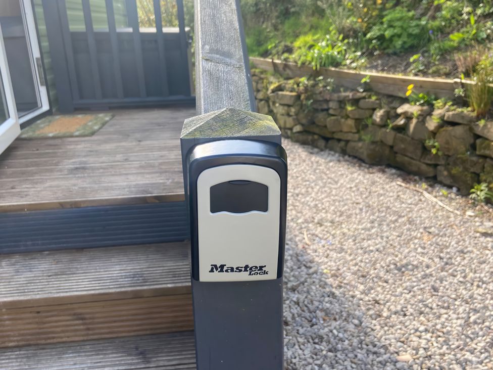 A lock box on a stair railing next to a stone wall at Coworth Deluxe Cabin with Garden