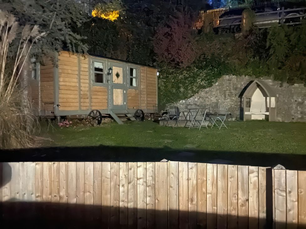 A wooden cabin beside a stone wall with chairs and table in the garden at Cozy Cabin Retreat in Newtown