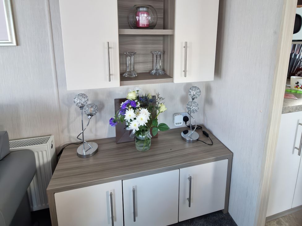 A cabinet with a vase of flowers and lamps in a living room at Caravan Sleeps 6 with Sea Views and Parking in Ayr