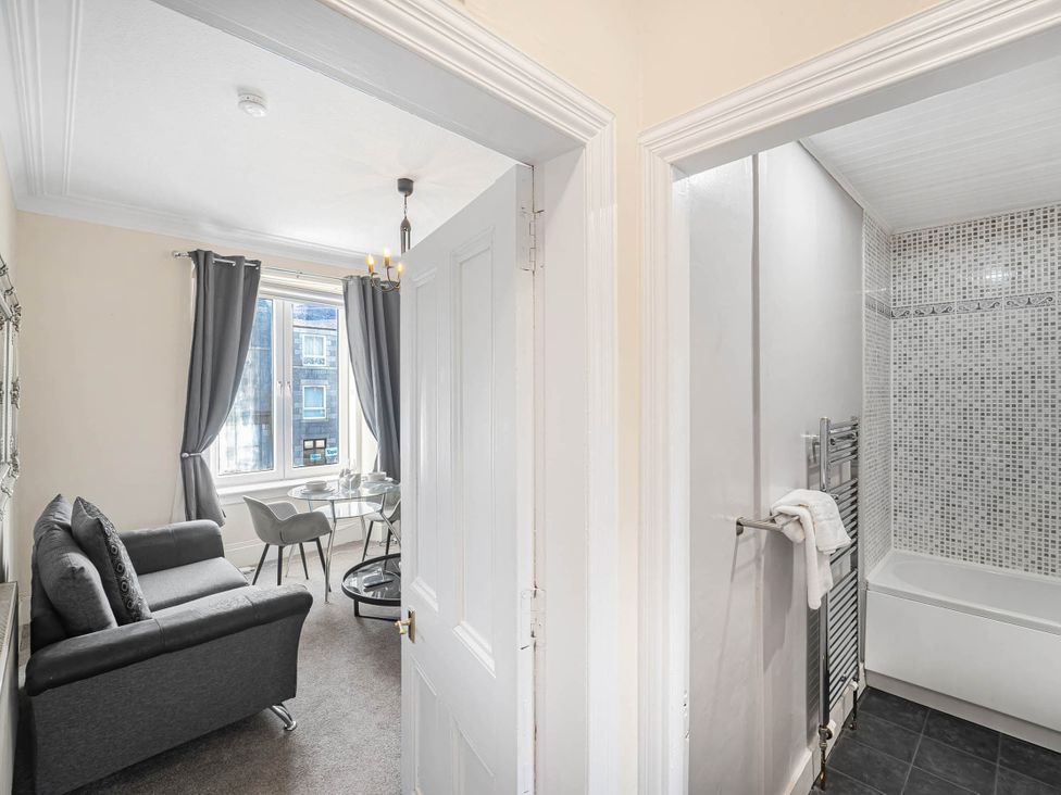 A living room with a sofa, table, and chairs next to a bathroom with a bathtub at Central Aberdeen flat Holburn St workspace parking in Aberdeen