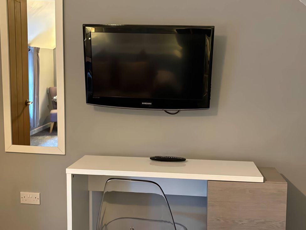 A TV mounted on a wall above a console table with a remote at Rural 2 double bedrooms Barn Mill Meece near Eccleshall