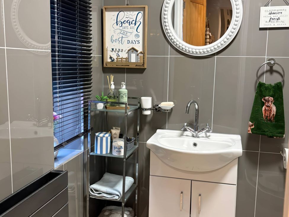 A bathroom with a sink, mirror, shelf, and decorative items at Rural 2 double bedrooms Barn in Mill Meece near Eccleshall