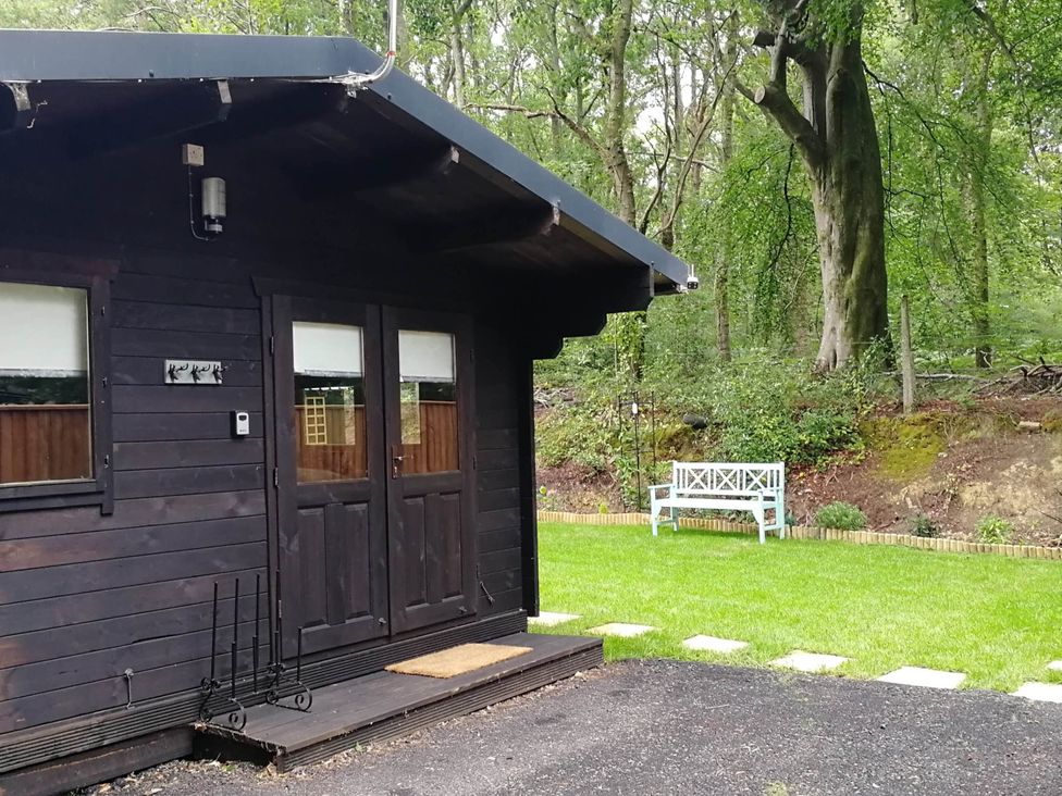 A wooden cabin with double doors and a bench in the garden at Forest Cabin Retreat-Sleeps 2-Garden, Wifi, Trails in Alderholt