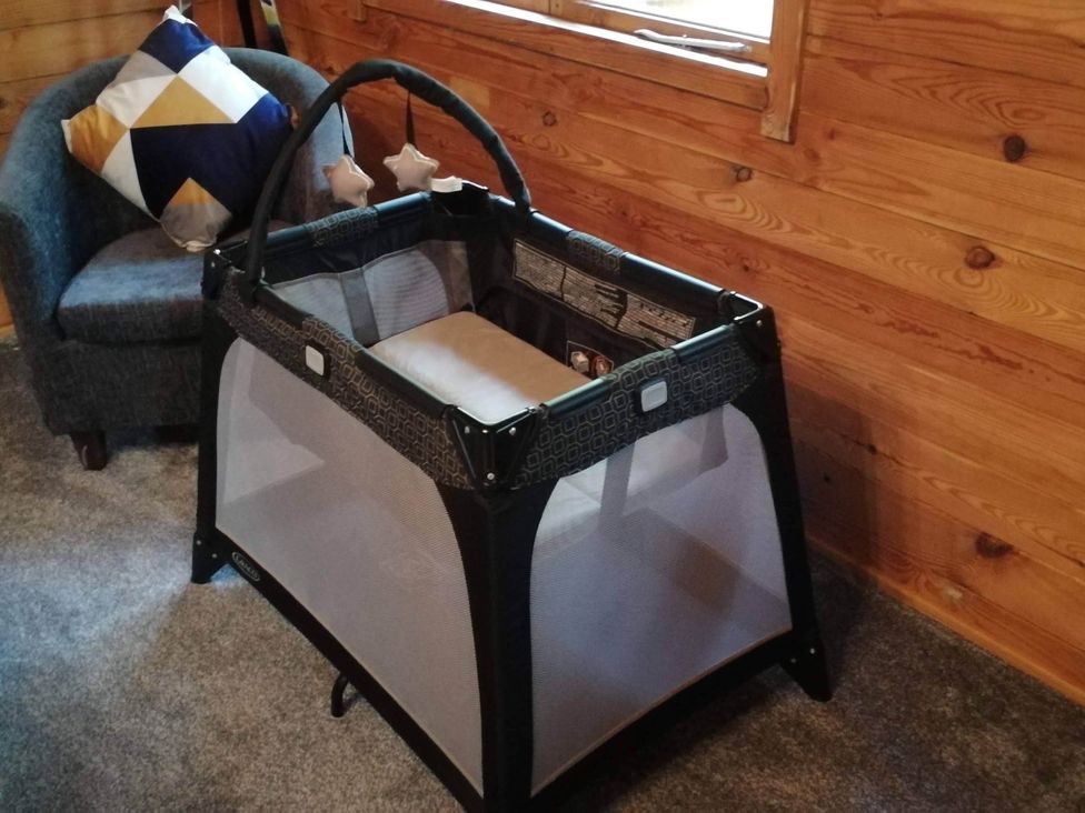 A playpen adjacent to an armchair in a living room at Forest Cabin Retreat-Sleeps 2-Garden, Wifi, Trails,Alderholt