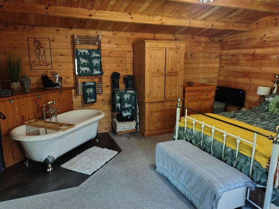 A bedroom featuring a bathtub, bed, and wooden furniture at Forest Cabin Retreat-Sleeps 2-Garden, Wifi, Trails, Alderholt