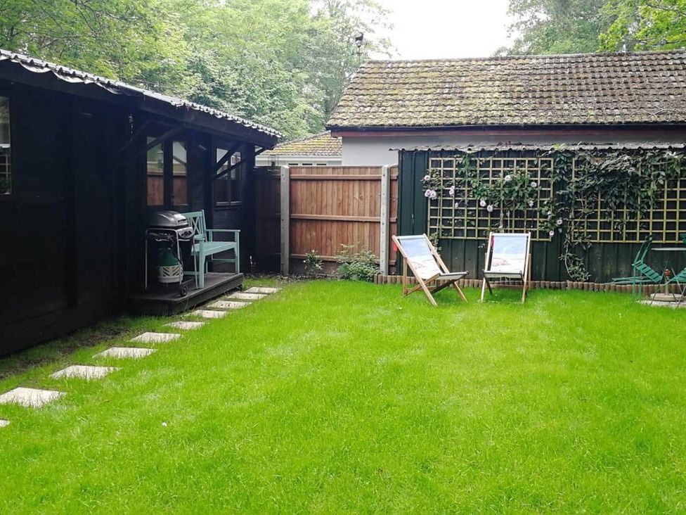 A garden with a lawn and deck chairs at Forest Cabin Retreat-Sleeps 2-Garden, Wifi, Trails in Alderholt