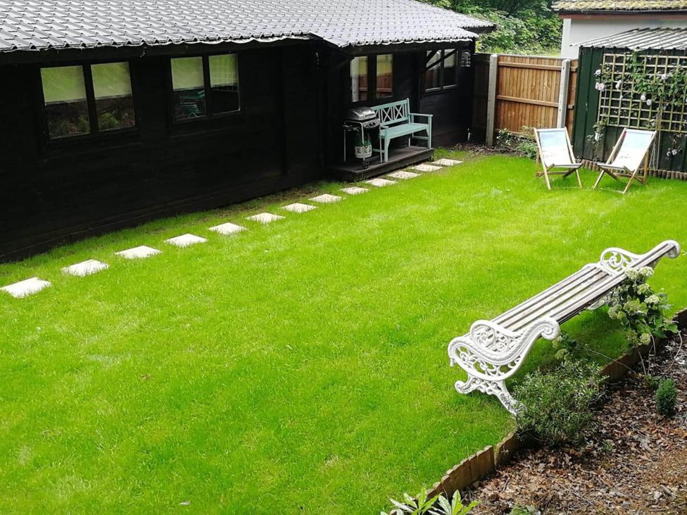 A garden with grass, a bench, stepping stones, and chairs at Forest Cabin Retreat-Sleeps 2-Garden, Wifi, Trails in Alderholt