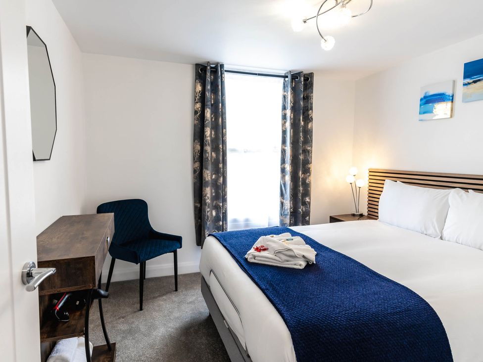 A bedroom with a bed, chair, and bedside table at Cosy 2-Bed Apartment in Nettleham