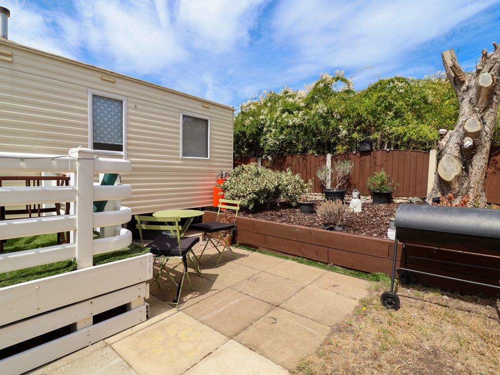 A garden with a caravan, table, chairs, and plants at Plot 594 Prestatyn