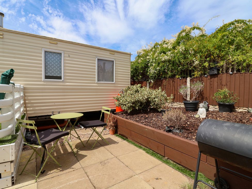 A garden area with a caravan, table, chairs and plants at Plot 594 Prestatyn